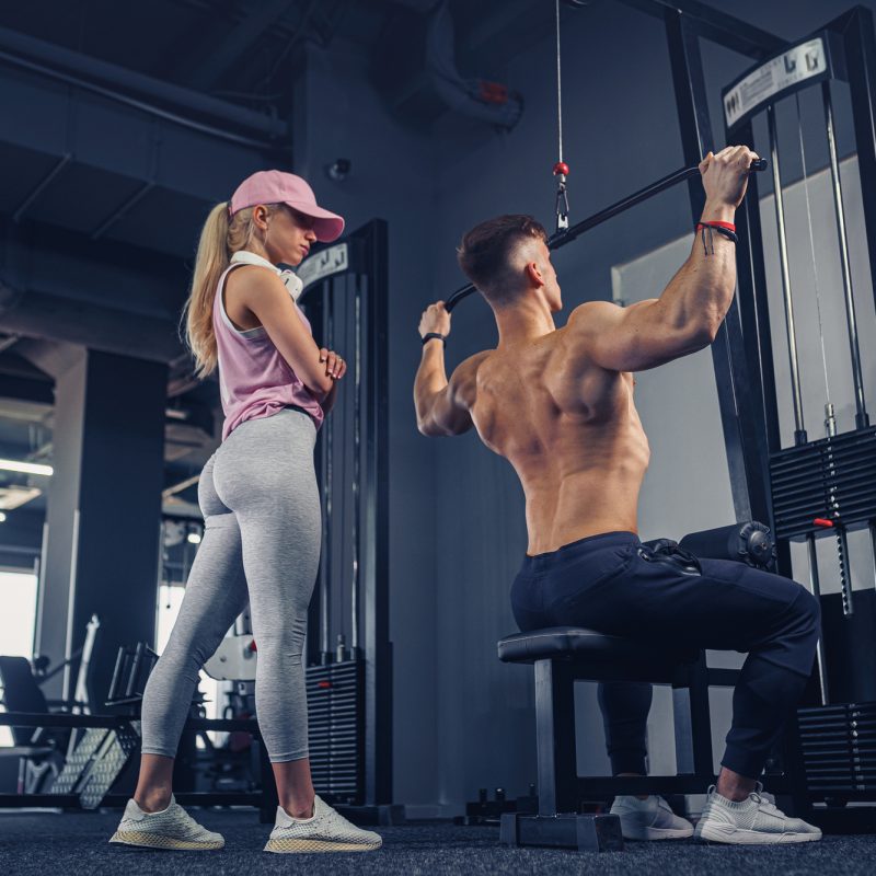young male bodybuilder doing heavy weight exercise while his girlfriend watching him.